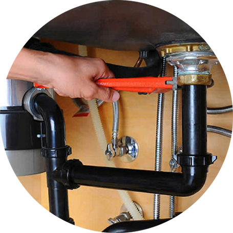 Plumber using a pipe wrench on a garbage disposal beneath the sink